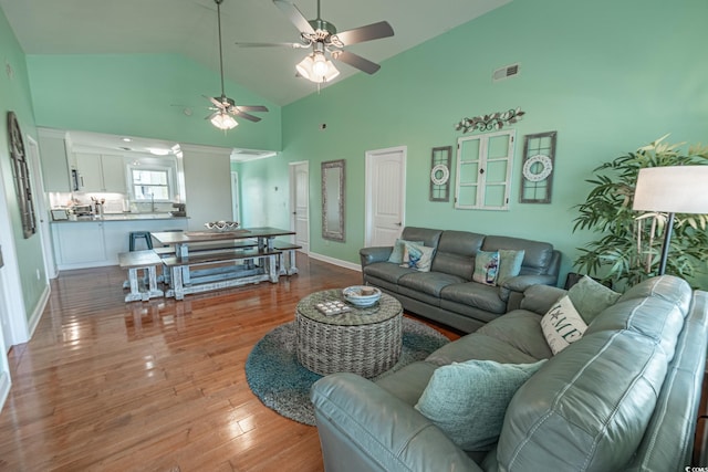 living area with high vaulted ceiling, ceiling fan, wood finished floors, and baseboards