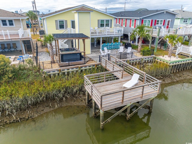 dock area with a deck with water view, stairs, a fenced backyard, a patio, and a jacuzzi