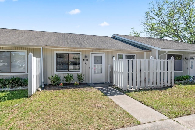 ranch-style house featuring a front lawn, roof with shingles, and fence