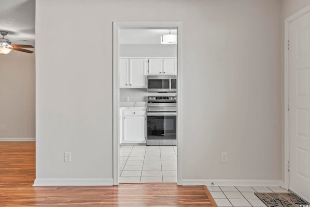 kitchen featuring a ceiling fan, white cabinetry, baseboards, appliances with stainless steel finishes, and light tile patterned flooring
