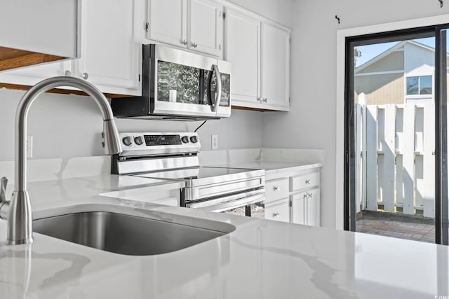kitchen with a sink, stainless steel appliances, white cabinetry, and light stone counters