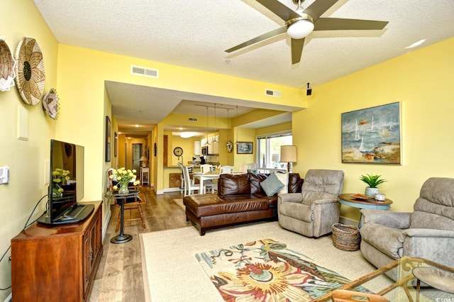 living room featuring a textured ceiling, ceiling fan, visible vents, and wood finished floors
