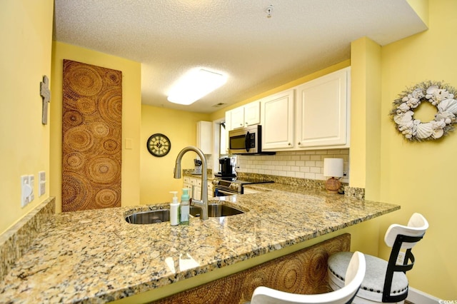 kitchen with light stone countertops, a sink, stainless steel appliances, white cabinetry, and decorative backsplash