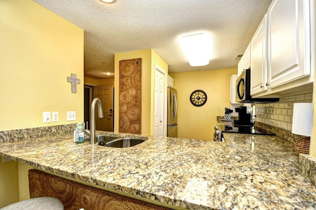 kitchen featuring light stone counters, a sink, freestanding refrigerator, a peninsula, and tasteful backsplash