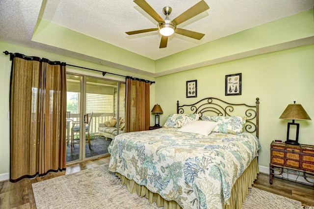 bedroom with wood finished floors, baseboards, access to outside, a textured ceiling, and a raised ceiling