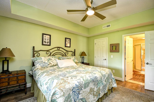 bedroom featuring ensuite bath, a ceiling fan, baseboards, wood finished floors, and visible vents