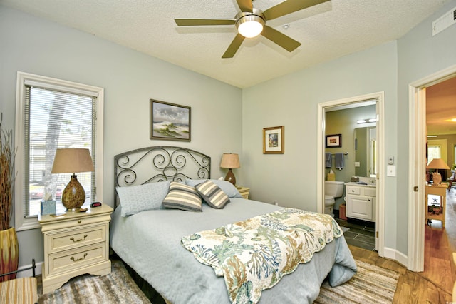 bedroom featuring connected bathroom, a textured ceiling, a ceiling fan, wood finished floors, and visible vents