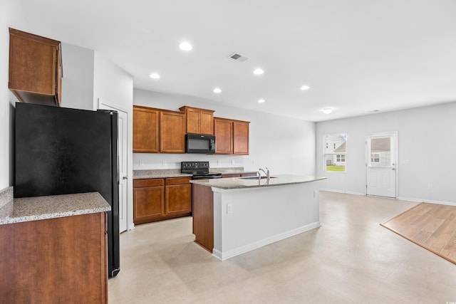 kitchen with a kitchen island with sink, brown cabinets, light stone counters, a sink, and black appliances