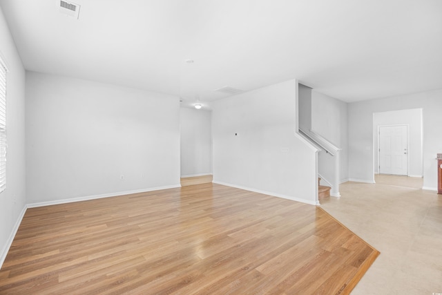 unfurnished living room with baseboards, visible vents, stairway, and light wood-type flooring
