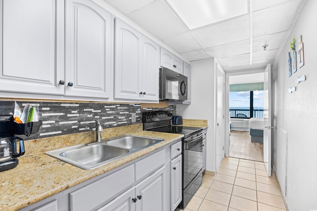 kitchen featuring light tile patterned flooring, a sink, white cabinetry, tasteful backsplash, and black appliances