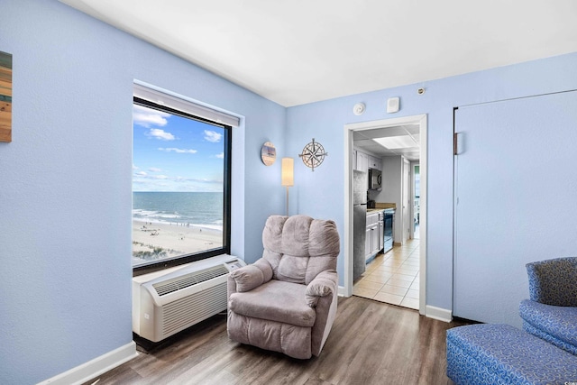 living area featuring baseboards, a wall mounted AC, a water view, and wood finished floors
