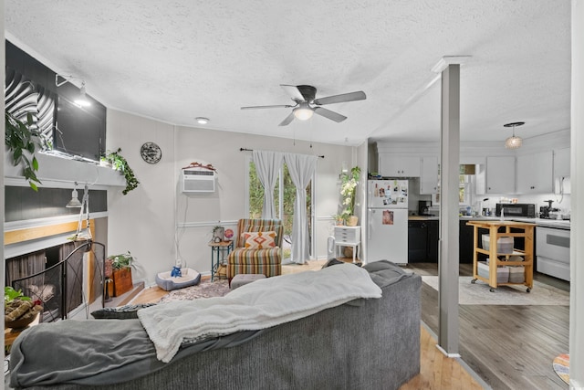 living room featuring a textured ceiling, ceiling fan, light wood-type flooring, and an AC wall unit