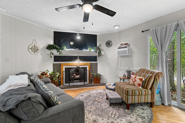 living area with a textured ceiling, ornamental molding, wood finished floors, a wall mounted AC, and a fireplace with raised hearth