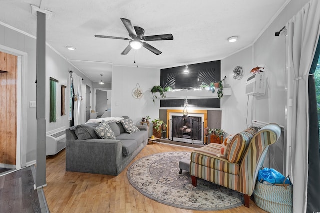 living room with hardwood / wood-style flooring, a fireplace with raised hearth, a ceiling fan, crown molding, and a textured ceiling