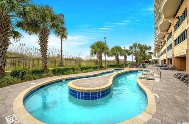 community pool with a hot tub, fence, and a patio area