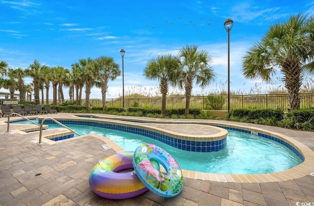 community pool with a hot tub, fence, and a patio