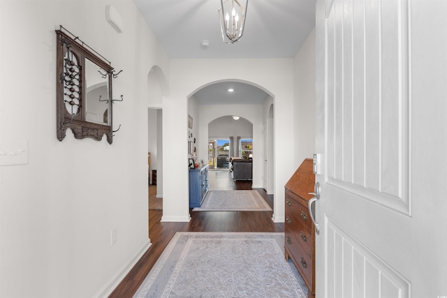 corridor with arched walkways, dark wood finished floors, baseboards, and a chandelier