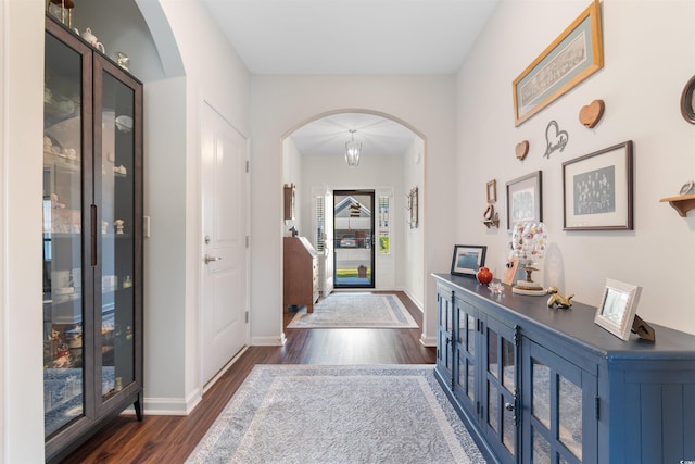entrance foyer with arched walkways, dark wood finished floors, and baseboards