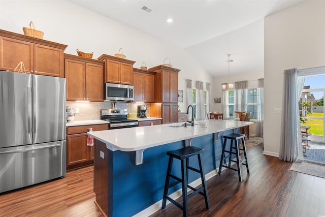 kitchen featuring stainless steel appliances, a sink, brown cabinets, vaulted ceiling, and dark wood finished floors