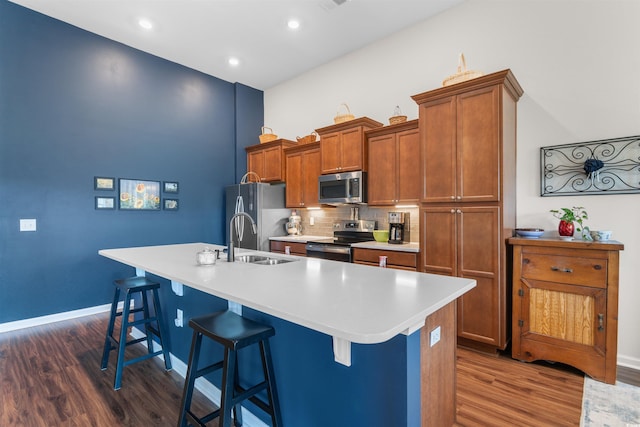kitchen featuring stainless steel appliances, dark wood-style flooring, a sink, an island with sink, and a kitchen breakfast bar