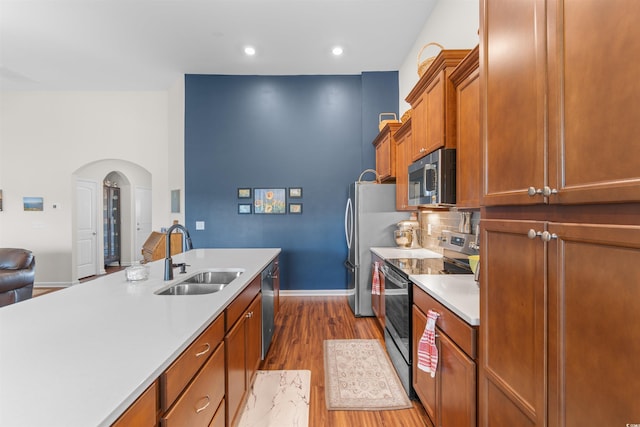 kitchen with appliances with stainless steel finishes, a sink, wood finished floors, light countertops, and baseboards