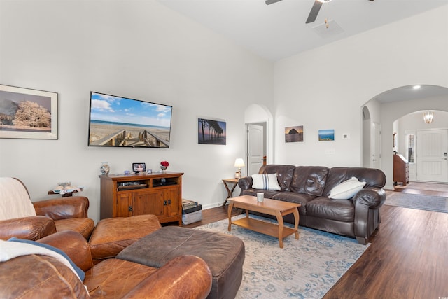 living room featuring arched walkways, wood finished floors, ceiling fan, a towering ceiling, and baseboards