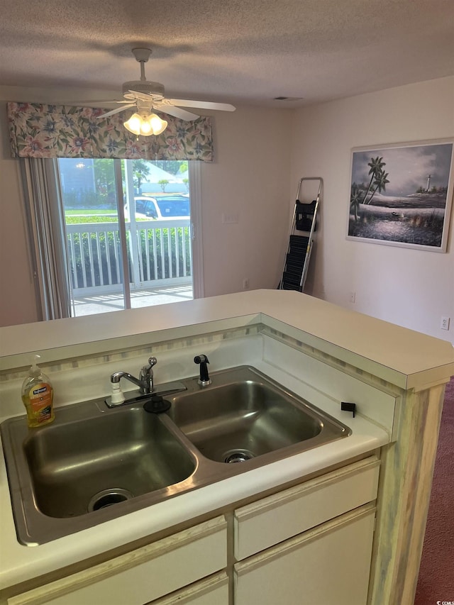 kitchen with a sink, light countertops, ceiling fan, and a textured ceiling
