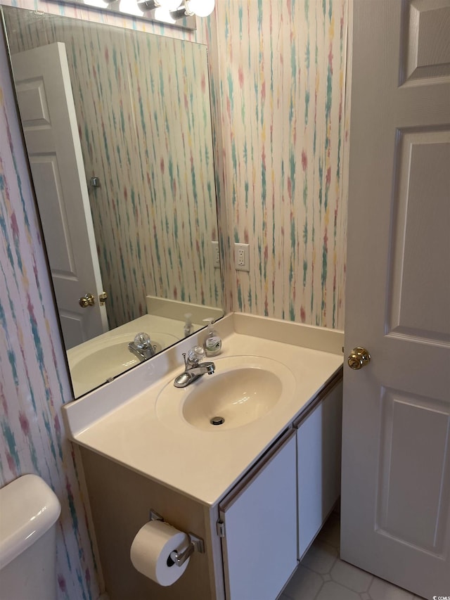 half bathroom with vanity, toilet, and wallpapered walls