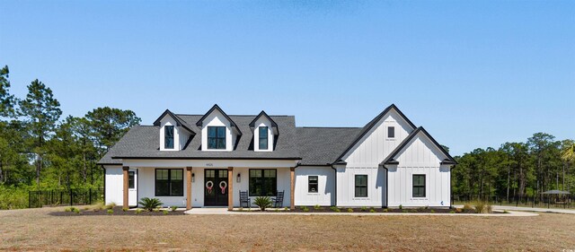 view of front of house featuring a front lawn, fence, roof with shingles, board and batten siding, and a porch