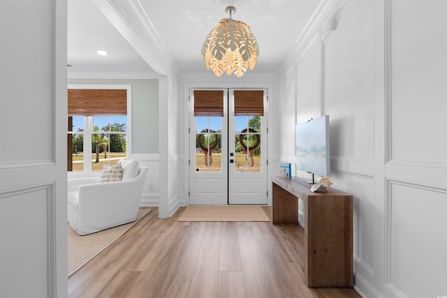doorway with crown molding, wood finished floors, a wainscoted wall, an inviting chandelier, and a decorative wall