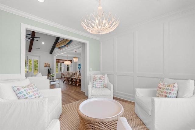living area with beam ceiling, light wood-style floors, a decorative wall, a chandelier, and ornamental molding