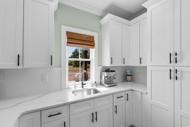kitchen featuring a sink, light stone counters, white cabinets, and tasteful backsplash