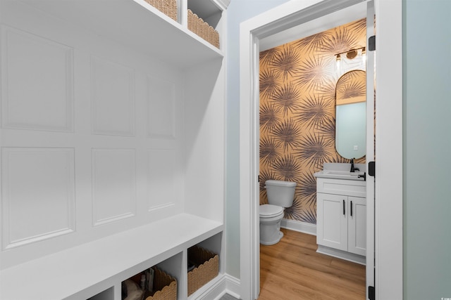 bathroom featuring wood finished floors, baseboards, vanity, toilet, and wallpapered walls