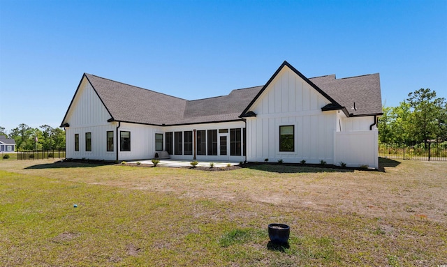 rear view of house featuring roof with shingles, fence, board and batten siding, and a lawn