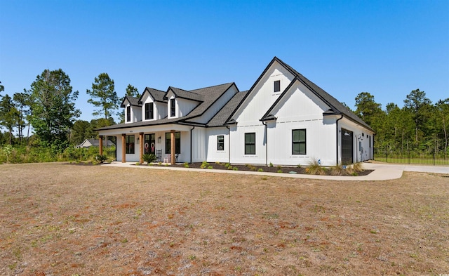 modern inspired farmhouse with a porch, an attached garage, fence, and a front lawn