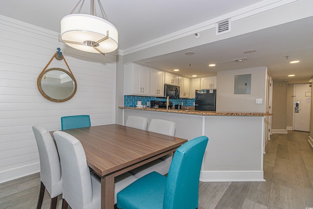 dining area featuring electric panel, visible vents, wood walls, baseboards, and light wood finished floors