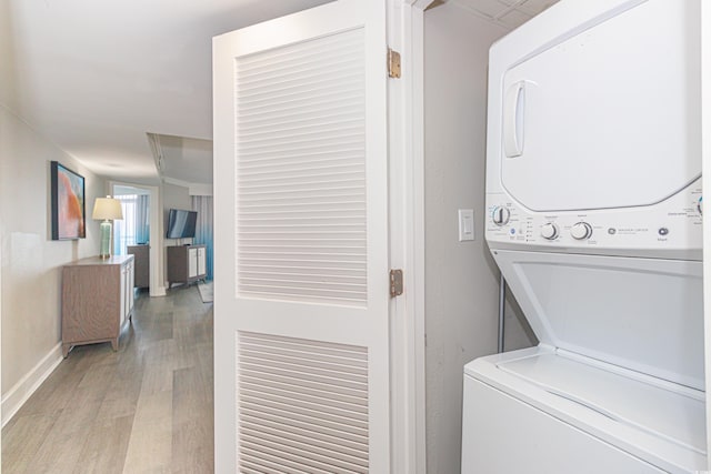 clothes washing area with laundry area, stacked washer and dryer, light wood finished floors, and baseboards