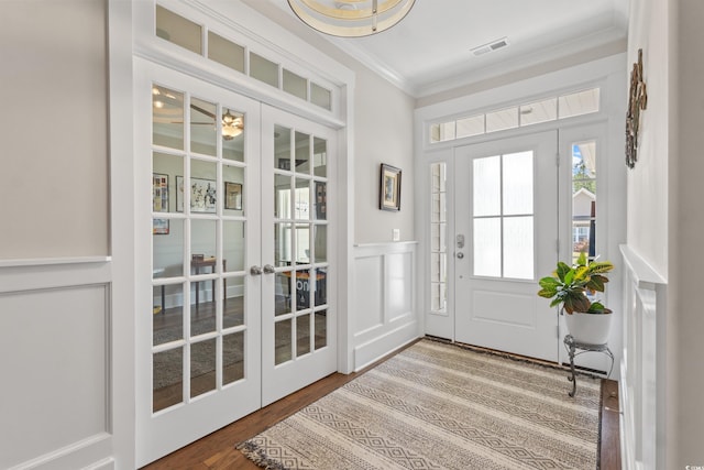 entrance foyer featuring a decorative wall, french doors, wood finished floors, visible vents, and ornamental molding