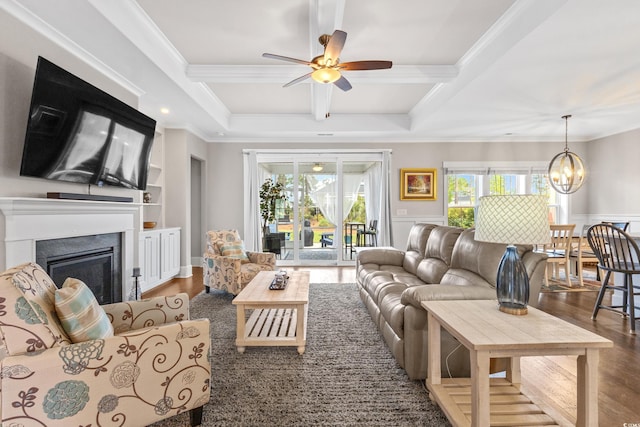 living area with a fireplace, wood finished floors, beamed ceiling, ceiling fan with notable chandelier, and ornamental molding
