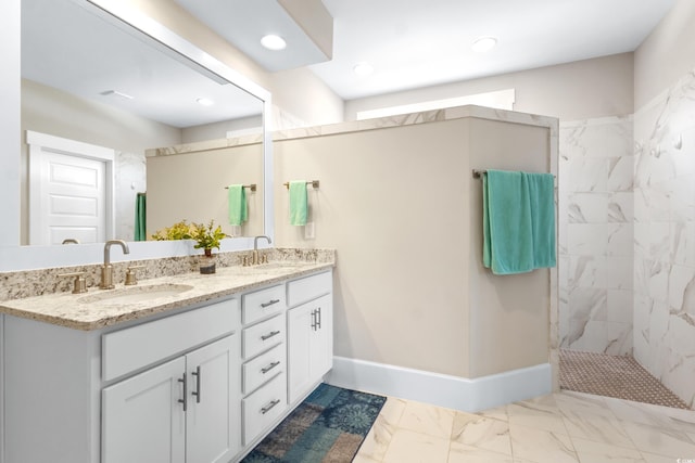 full bath featuring double vanity, baseboards, a tile shower, and a sink