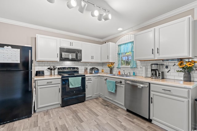 kitchen with black appliances, a sink, light countertops, crown molding, and light wood-style flooring