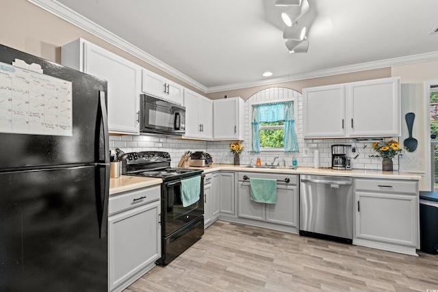 kitchen with black appliances, ornamental molding, light countertops, light wood-style flooring, and decorative backsplash