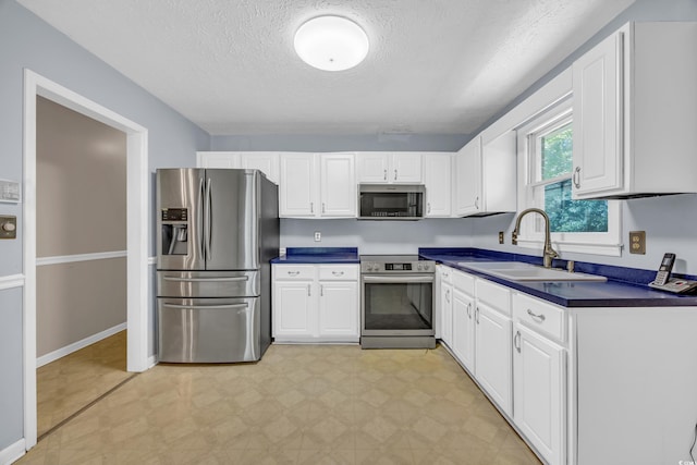 kitchen with stainless steel appliances, a sink, dark countertops, light floors, and a textured ceiling