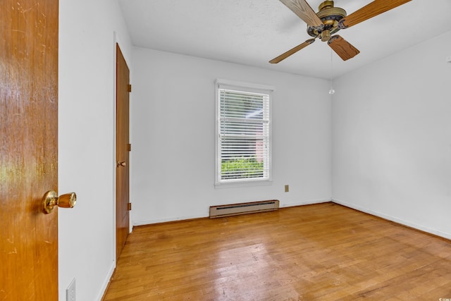 spare room featuring a baseboard heating unit, wood finished floors, a ceiling fan, and baseboards