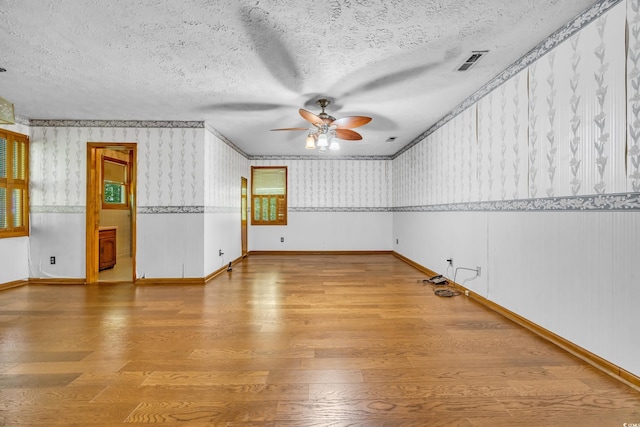 spare room featuring a ceiling fan, wallpapered walls, wood finished floors, baseboards, and a textured ceiling