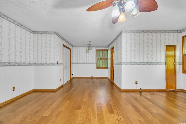 unfurnished living room with wallpapered walls, a ceiling fan, wood finished floors, baseboards, and a textured ceiling