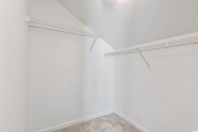 walk in closet with light colored carpet and lofted ceiling