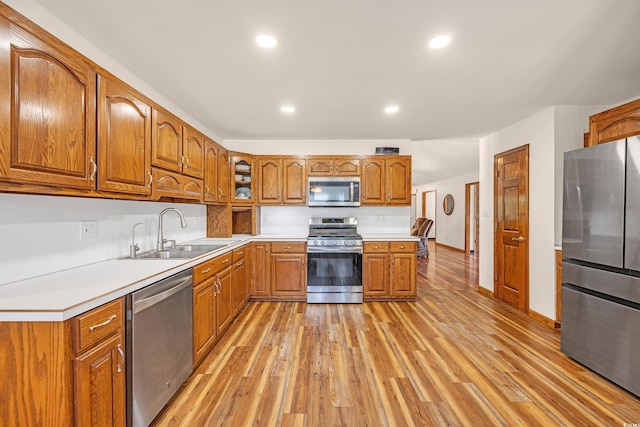 kitchen with light wood finished floors, appliances with stainless steel finishes, brown cabinets, and a sink