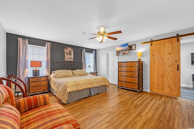 bedroom featuring a barn door, light wood-style flooring, and ceiling fan