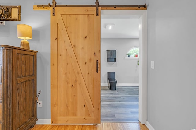 corridor with a barn door, wood finished floors, and baseboards